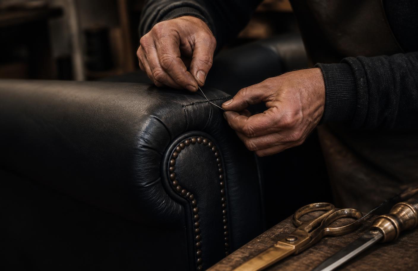 Craftsman's hands stitching the arm of a black leather sofa